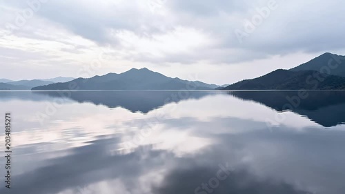 Calm lake surface reflecting layered mountains and clouds in a peaceful natural landscape