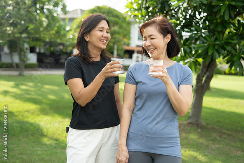Two mature Asian women drinking water outdoors