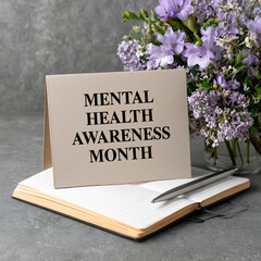 Mental Health Awareness Month card with an open notebook, pen, and purple flowers on a grey background, promoting well-being and support.