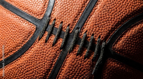 Extreme macro close-up of an orange basketball surface featuring pebbled leather texture, black rubber channels, and detailed black stitching.