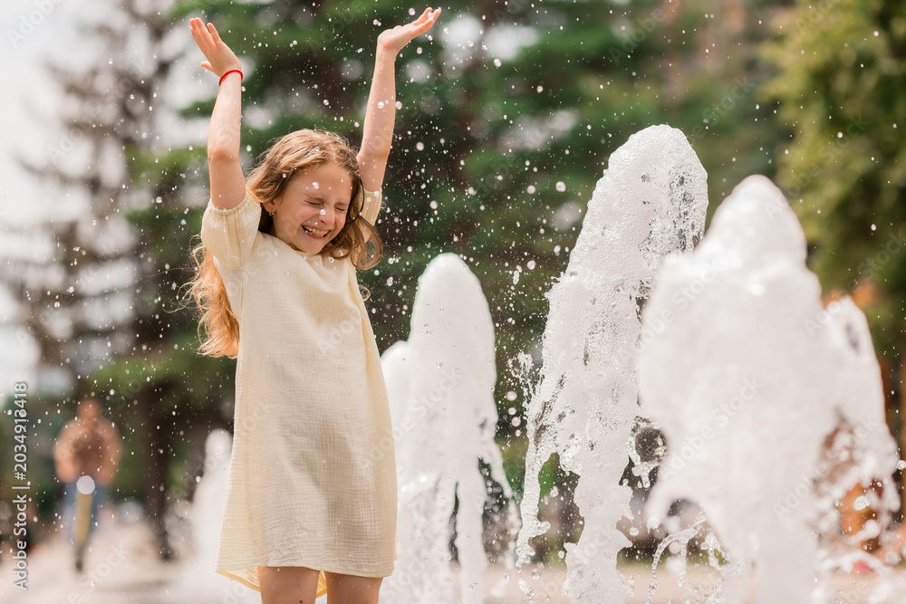 Carta da parati little girl enjoys splashing in the city fountain in the summer