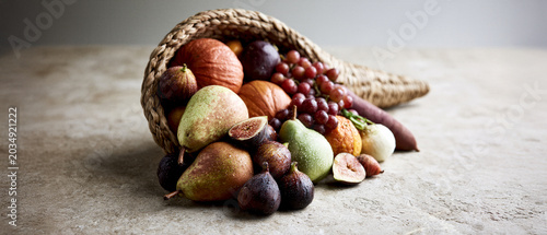 Cornucopia overflowing with fruits and vegetables on rustic background  