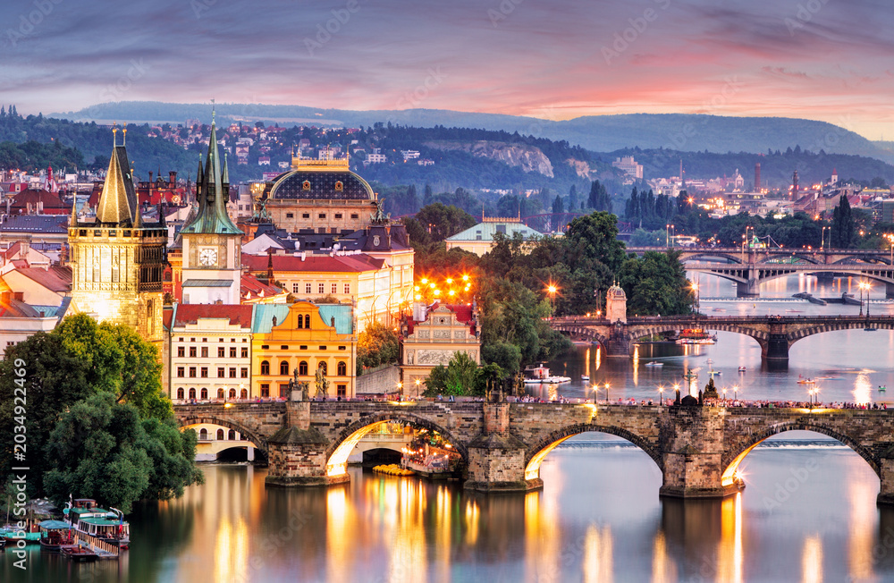 Obraz premium Twilight cityscape featuring multiple bridges over a river in Prague skyline, with historic buildings and street lights.