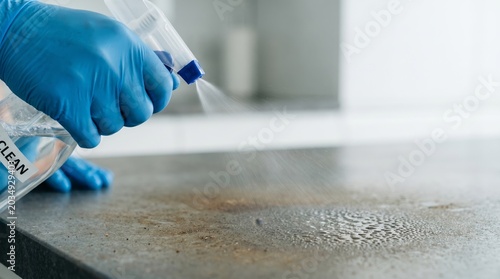 Close up of a gloved hand spraying disinfectant sanitizer on a dirty surface to clean virus contamination.
