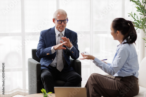 Senior businessman making a stop gesture, signaling refusal or disagreement during a professional meeting with a young female colleague in an office setting