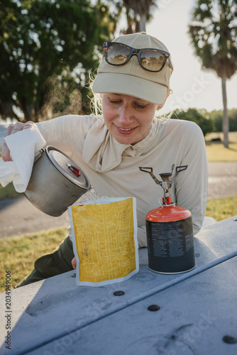 woman pours water into backpacking meal at campgound
