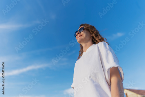 Konstfotografi Beautiful millennial girl smiling and looking away on a bright sunny day, view from below