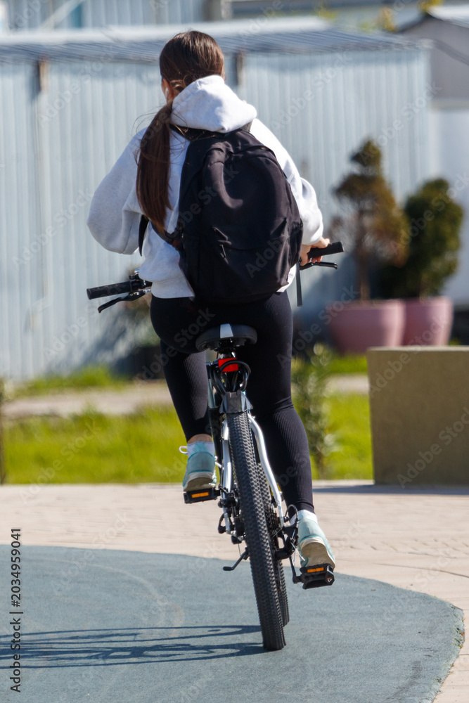 Obraz premium Back view of cyclist on paved path near modern buildings and plants