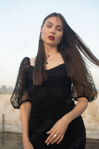 Beautiful and sensual young woman in a dress on a building rooftop in the golden hour