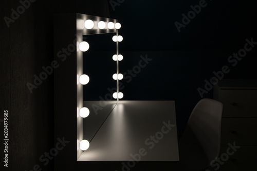 White modern vanity table with light bulbs illuminated in a dark room in home bed room.