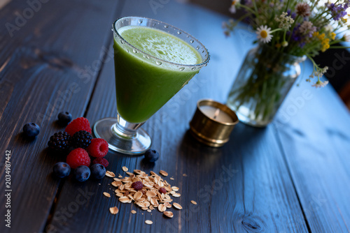 Healthy green smoothie with fresh berries and oats on dark wooden table