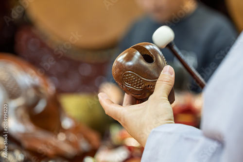 close up shot of hands holding wooden carved fish shaped prayer block ready to strike