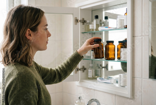 Side view of a young woman placing blank amber vitamin bottles inside a bathroom medicine cabinet