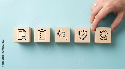 Hand placing a wooden block with a quality assurance icon in a row of professional business compliance symbols