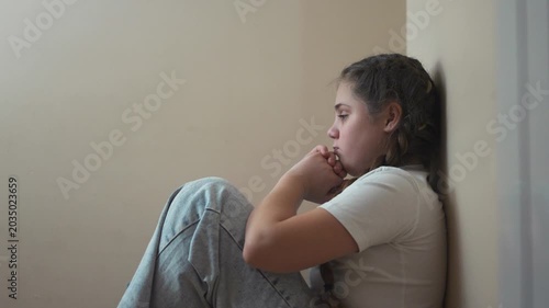 Young girl sitting on the floor. Sad child sits on a corner and is punished. A teenage girl is traumatized by a violent incident. A little lifestyle girl sitting on the ground.