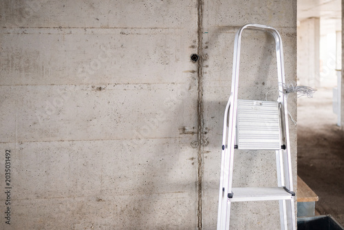 Photos A metal foldable stepladder leans against a raw, unfinished concrete pillar