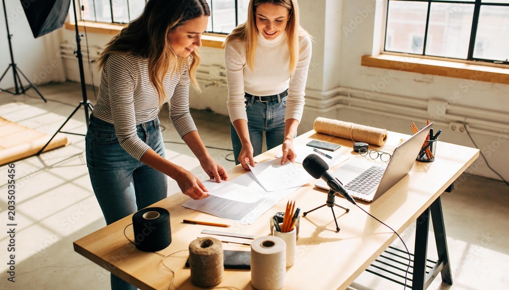 Naklejka premium Leaning pair arranging papers on wooden table in loft, wearing striped and white tops with jeans