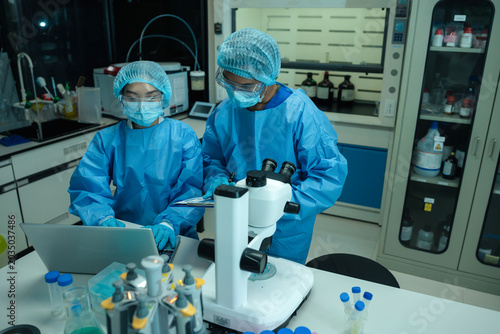 Tableau sur toile Asian team researchers examining natural water sample for contaminants and microplastics next to laboratory bottle