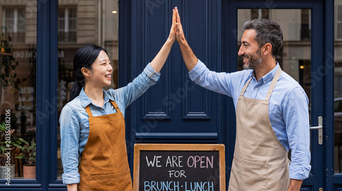 Fotografie Happy diverse small business owners giving high five in front of their successful cafe or restaurant