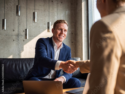 Fotografija Confident businessman in a suit shaking hands with an associate, finalizing a new business partnership agreement