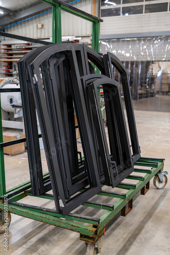 Fenêtres cintrées en aluminium noir prêtes à être installées, stockées dans un atelier de fabrication de menuiseries sur mesure.