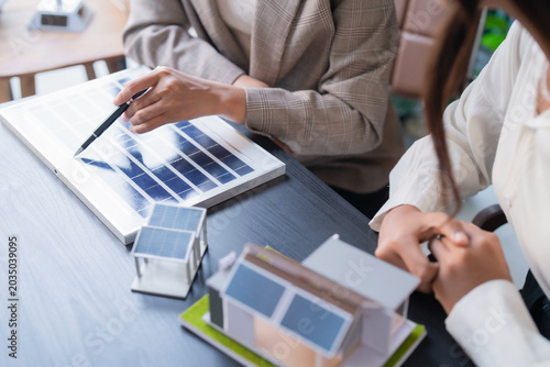 Asian sales consultants presenting solar energy solution using house model for client consultation