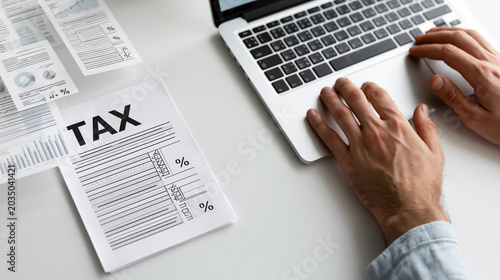 Tax Return Preparation: A person's hands are shown typing on a laptop keyboard next to a tax form and some documents, signifying tax preparation and financial management.