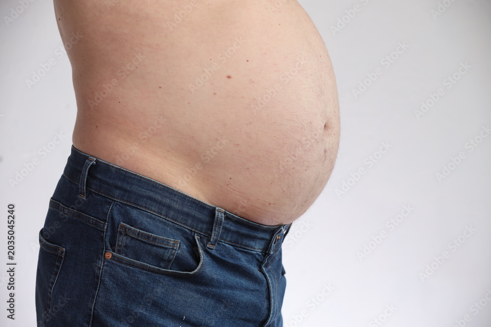 Naklejka premium Overweight man with belly in blue jeans. Concept of obesity, unhealthy lifestyle, excess weight and diet problems. Isolated on white background.