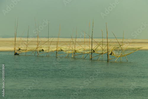 A row of traditional bamboo fish traps silhouette across a calm river