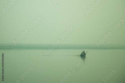 Two fishermen cast a long net across a misty river