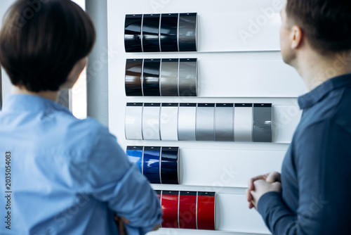 Couple making a decision on new car exterior paint, looking at color samples on display at an automotive showroom