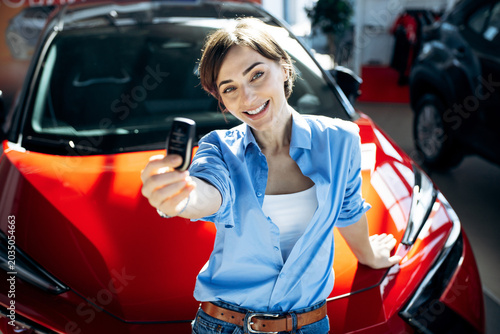 Tableau sur toile Happy woman holding new car keys, celebrating successful vehicle purchase at a d