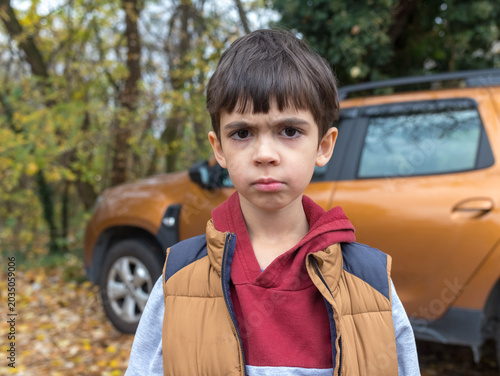 Upset Little Boy in Autumn Park Looking Grimly at Camera