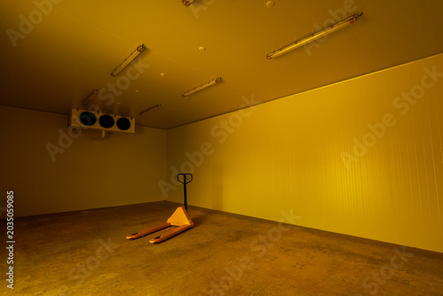 Empty yellow cold storage warehouse room with solitary manual pallet jack on concrete floor expressing eerie lonely abandoned atmosphere inside industrial facility