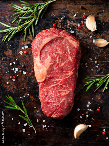 Tableau sur toile Raw ribeye beef steak with fresh rosemary garlic sea salt and peppercorns on dark rustic background for gourmet cooking concept