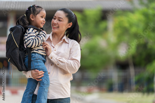 happy mother holding little daughter with a backpack, smilling and talking together on her first day of school