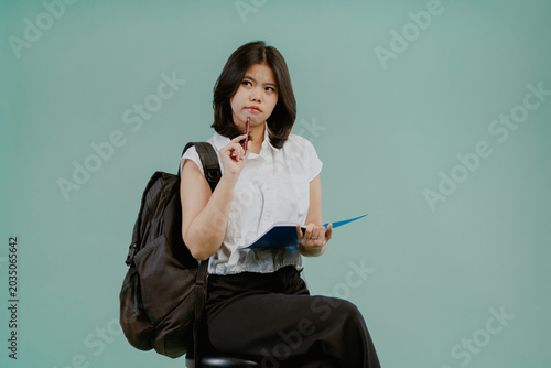 Pensive smart young asian girl thinking about something isolated on light green studio background.