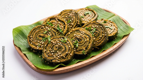 Rolled steamed savory parcels made from colocasia leaves, sprinkled with white sesame seeds