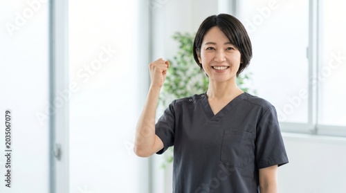 Smiling Asian female medical professional in scrubs making a fist gesture.