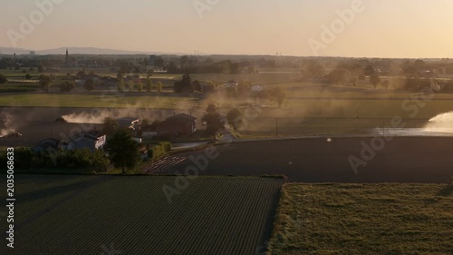 Agricultural activity in Emilia Romagna Pianura Padana Italy with sprinkler irrigation and soil tillage producing dust across cultivated fields revealed by drone yaw pan to left aerial shot