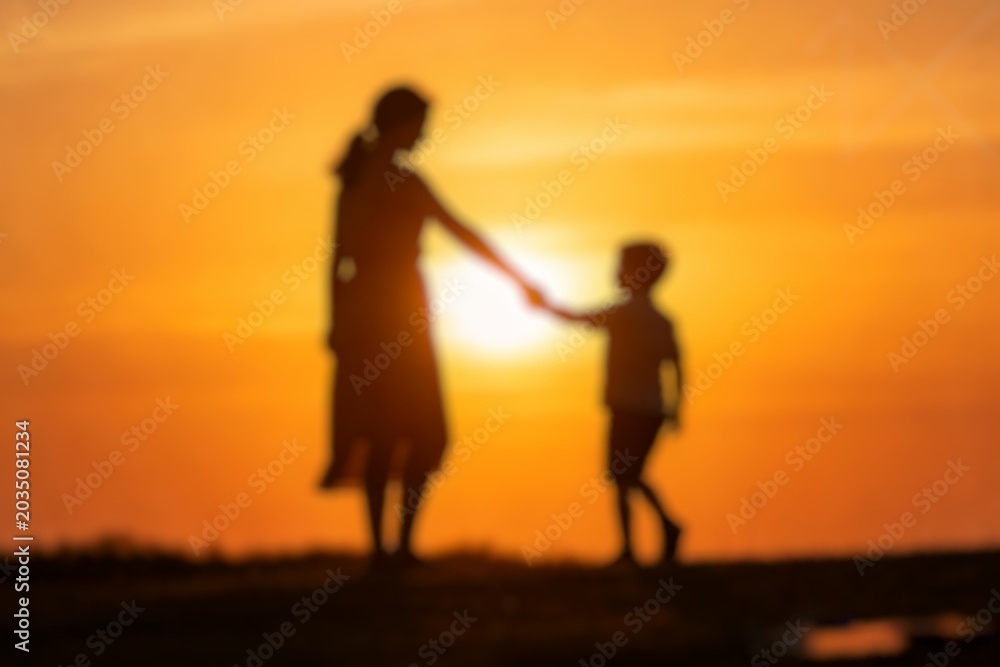 Fototapeta premium Blurred silhouette of a mother and child holding hands during a warm sunset, symbolizing love, care, and family connection.