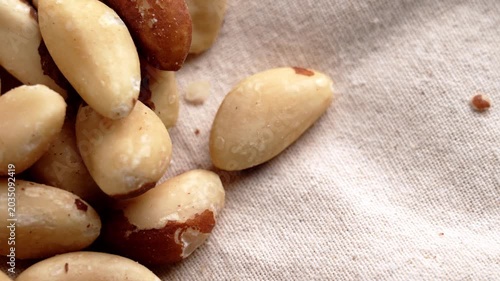 Fingers selecting a Brazil nut from a pile of mixed kernels on textured fabric surface. Concept of healthy snacks