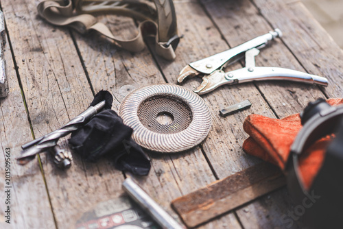 Assorted workshop tools including welding helmet and cutting discs placed on a wooden stool outdoors. Industrial DIY and metalworking equipment in natural light.
