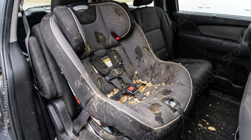 Child car seat heavily soiled with food crumbs stains and residue inside rear passenger area of vehicle interior
