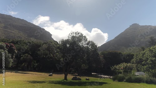 Clouds moving at high speed behind South African mountains with scenic park with trees swaying in foreground. Muizenberg, Cape Town, South Africa. 