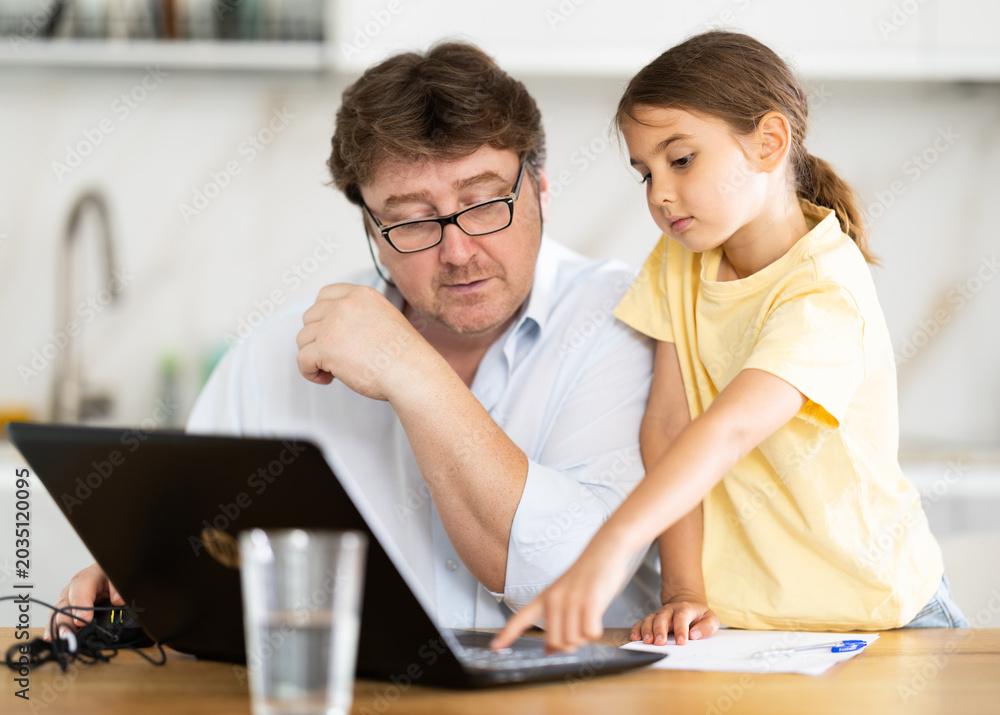 Fototapeta premium Little daughter shows her father how to use laptop
