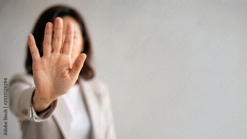Obraz premium Businesswoman extending hand in a stop gesture against a gray background.