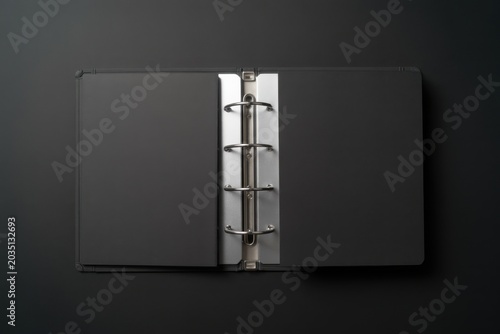 A sleek black binder lies open on a dark surface showcasing its silver rings.