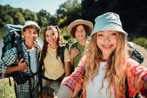 Bilde på lerret Smiling teenage friends taking a selfie on a sunny lakeside hike with backpacks