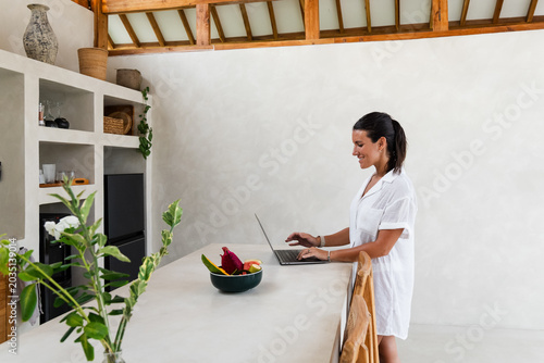 Foto Woman smiling while typing on a laptop, working remotely from a kitchen counter